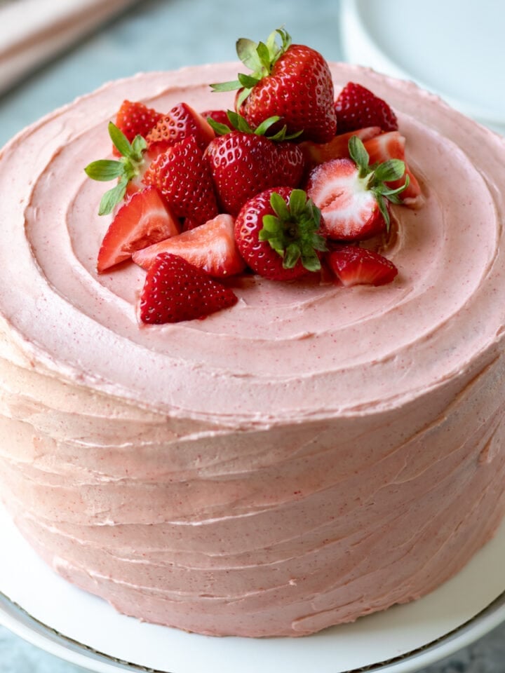whole 3-layer cake decorated with pink vegan frosting and strawberries on top