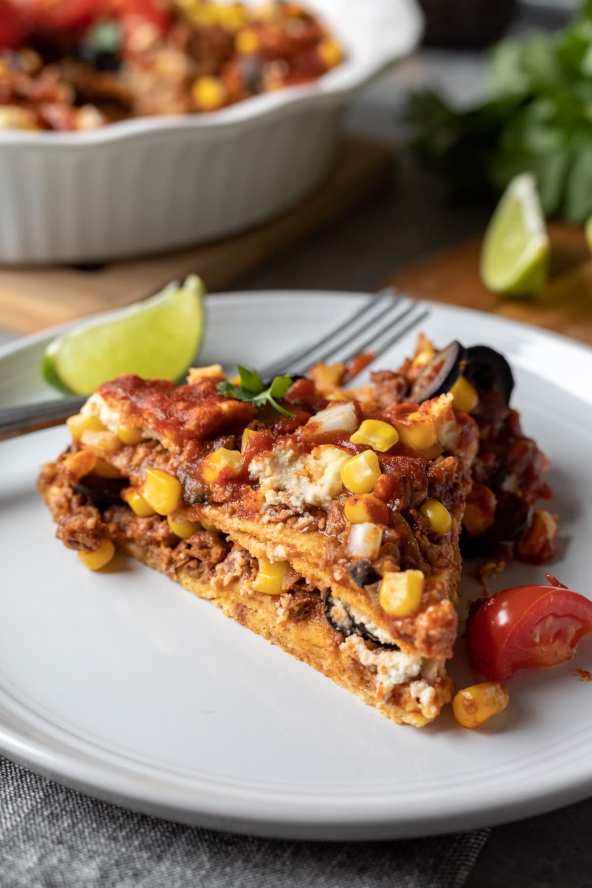 A slice of enchilada casserole on a plate with a lime wedge.