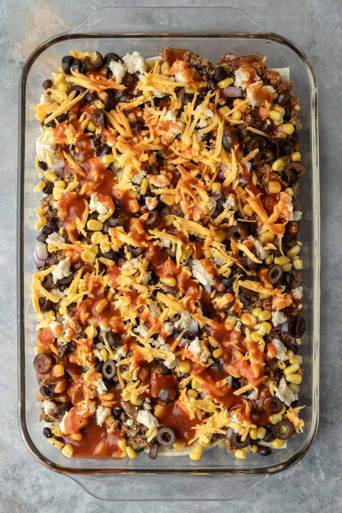 Layering two types of vegan cheese and enchilada sauce.